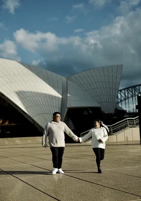 Walking hand in hand beneath the sails of the Sydney Opera House.