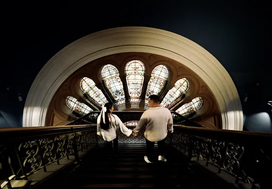 Hand in hand on a staircase beneath a great stained glass arch.